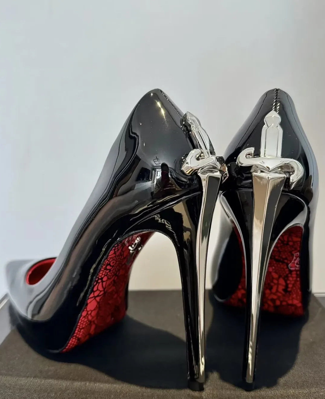 Black high-heeled shoes with red soles and silver straps on a gray surface, featuring the Cesare Paciotti brand.